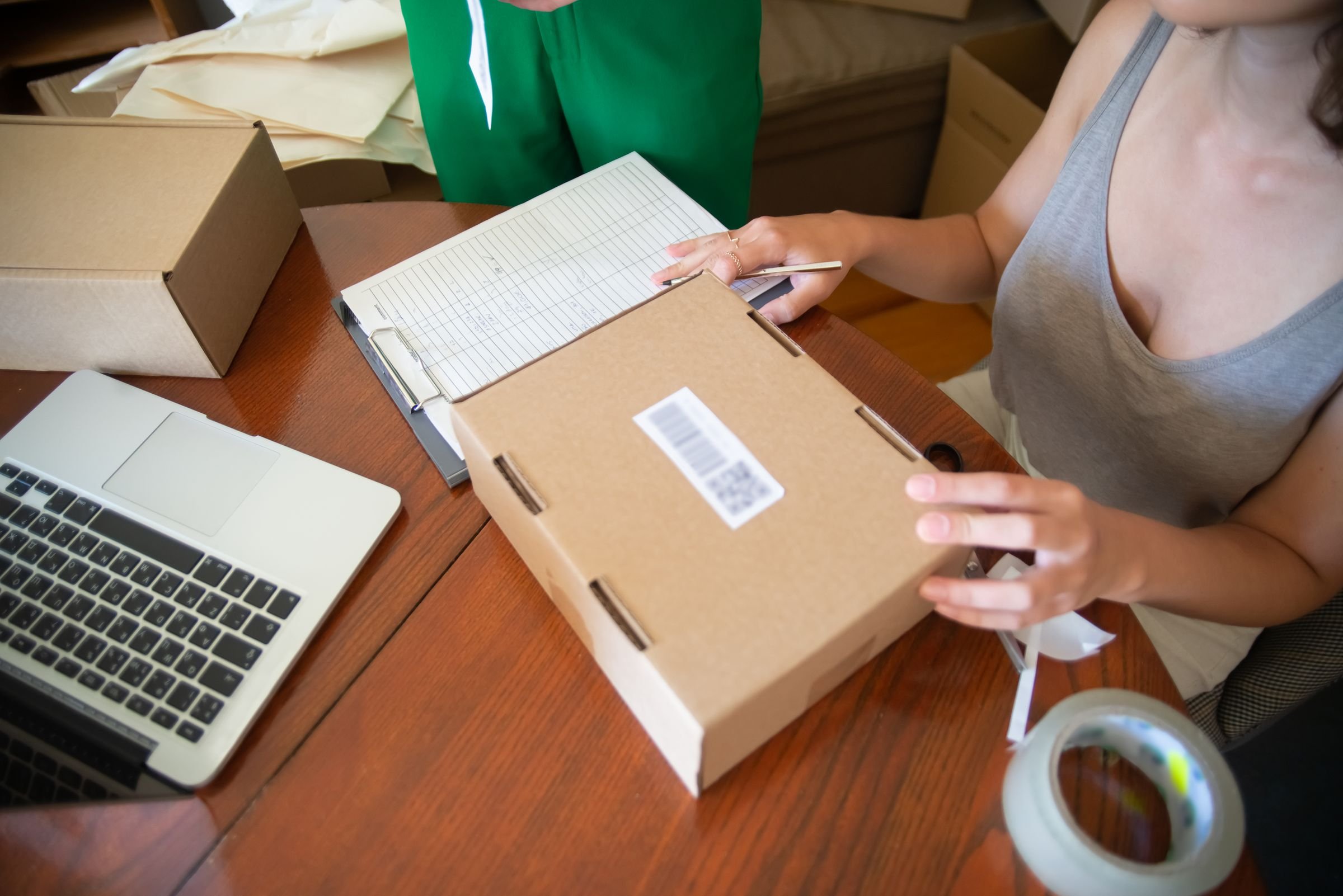 Two people packing an online order into a box beside a laptop