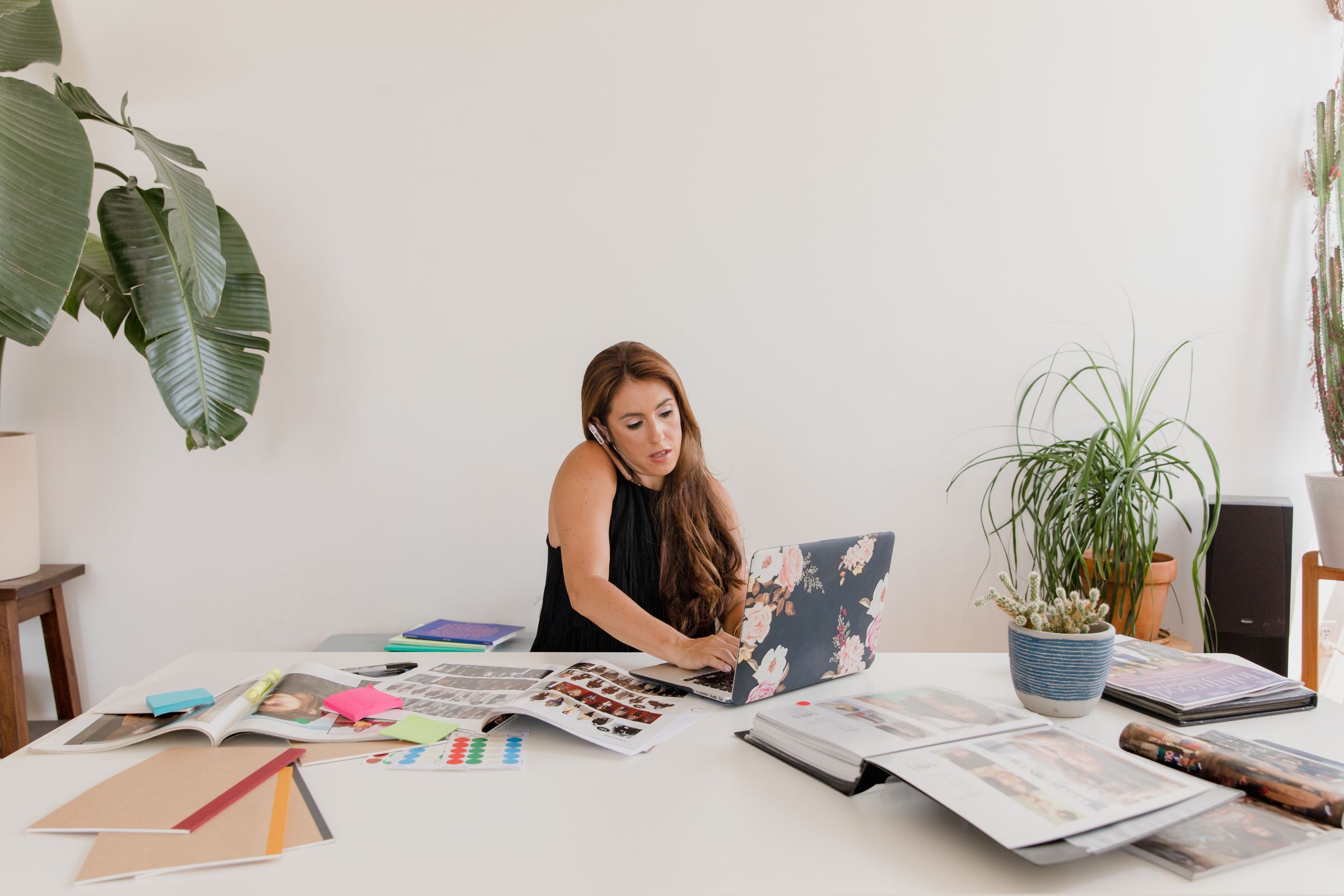 A small business owner on a phone call while typing on a laptop, her desk covered in samples and paperwork