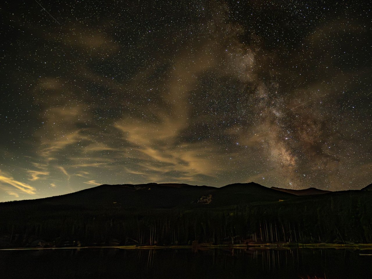 The Milky Way arching over a dark mountain ridge at night.