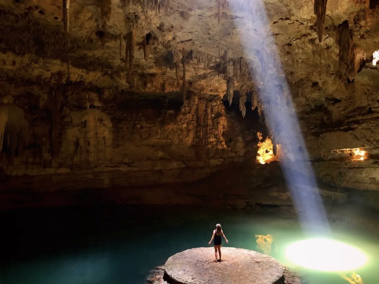 Sunlight pouring into a cavern pool above a stone platform.