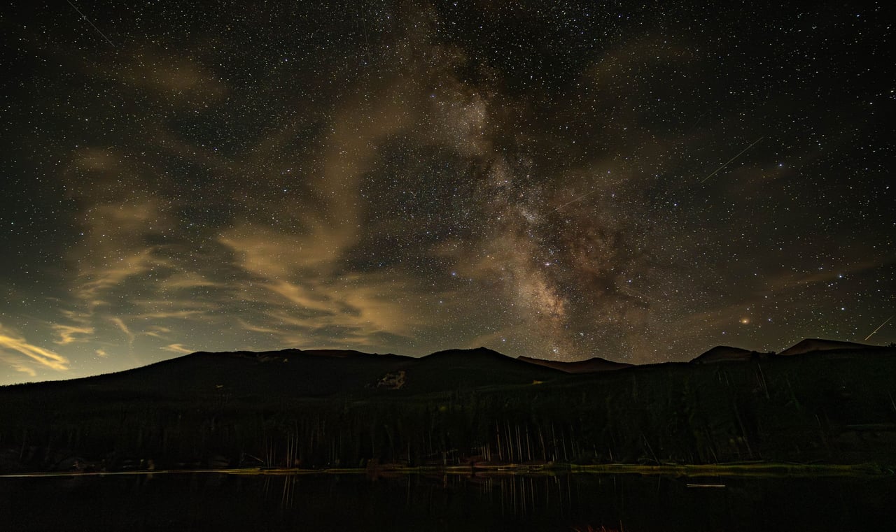 The Milky Way arching over a dark mountain ridge at night.