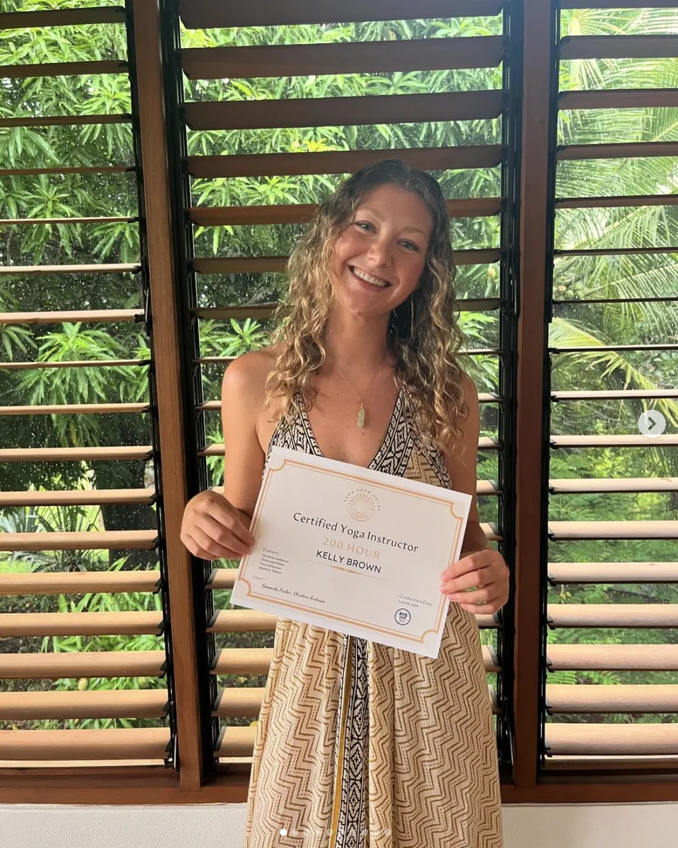 Kelly Brown smiling, holding her 200-hour yoga instructor certificate in Costa Rica.